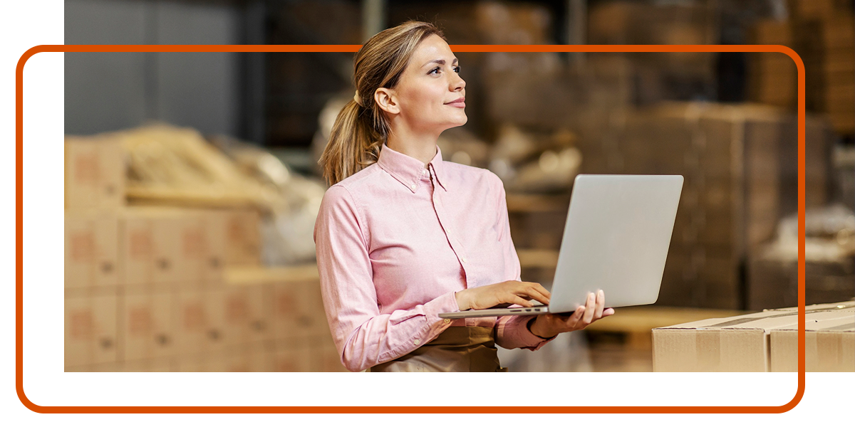 a woman using her laptop in a warehouse, leveraging their TMS software